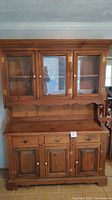 Front view of wooden china cabinet with three glass paneled doors on top and three wood doors below, showing rustic finish with some scratches.