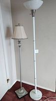 Pair of floor lamps side by side: one ornamental with fabric shade, one white torchiere style