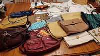 Photo of 22 assorted vintage purses laid out on a wooden surface showing variety of colors and styles, including leather, quilted, fabric, and printed materials.