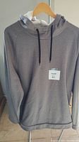 Front view of grey hooded sweatshirt with black drawstrings and white hood lining hanging on a hanger.