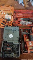 Four used electric power tools in various plastic carrying cases on a carpeted floor