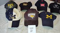 Overview of eight sports hats with various local and collegiate logos on table.