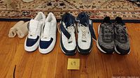 Three pairs of sneakers: white and blue Nike Air high-top size 14 used, white and blue Nike Air low-top size 13 unused, black and grey The North Face sneaker approx size 10.5 lightly used.
