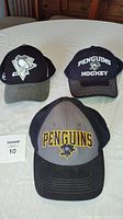 Three Pittsburgh Penguins baseball caps displayed on table, front and top views showing logos and condition