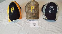 Front view of three Pittsburgh Pirates baseball hats arranged side by side on a white surface, showing logos and colors.