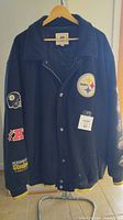 Front view of the Steelers heavy jacket showing snap buttons, Pittsburgh Steelers circular logo patch on left chest, sport patches on sleeves including helmet and AFC logos, ribbed yellow-trimmed cuffs and hem.
