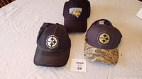 Photo showing three caps: two Pittsburgh Steelers caps and one Towson University cap, arranged on a table with a lot card