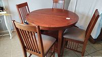 Tall round wood grain dinette table with 4 matching tall chairs with fabric cushions arranged around it.