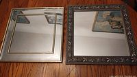 Two square wall mirrors side by side on wooden floor showing the grey carved frame mirror and the gold metal trim frame mirror