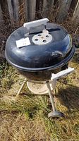Side view showing black kettle grill with white handles and wheels on grass outdoors.