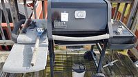 Front view of Weber gas grill showing side shelf with spatula and grill lid with thermometer and branding.