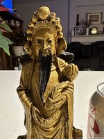 Close-up of the front of brass figure showing detailed carved face, long black beard, ornate gown and headdress, holding a child.