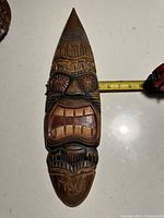 Close-up photo of the tiki mask with a measuring tape showing about 8 inches in width.