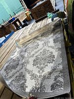 Photo of rectangular floral area rug spread on wooden pallet showing detailed flower pattern and one corner being lifted to show the backing and edges.