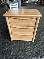 Front view of bedside table showing three drawers and wood finish.