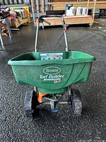 Front view of green Scotts Turf Builder broadcast spreader showing overall shape, wheels, and handlebar.