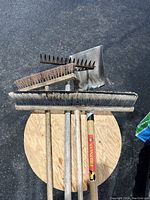Overview of the four cleaning and garden tools on wooden stool, showing bristles and metal heads.