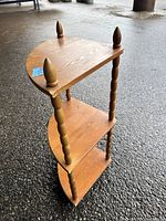 Full view of the wooden corner shelving unit showing three-tier triangular shelves with turned spindle supports and finial toppers at the corners.