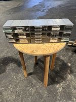 Front view of the craft organizer placed on a wooden stool, showing all closed drawers and black plastic frame.