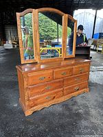 Overall wood dresser with seven drawers and attached three-panel arched mirror. Shows side angle and drawer design.