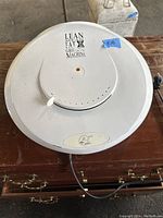 Top view of the white round electric grill lid with vent holes, control knob, and branding sticker on top.