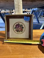Front view of the floral embroidery framed artwork with measuring tape showing width around 21.5 cm or approx 8.5 inches.