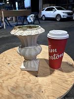 Flower pot and a large coffee cup side by side on a wooden surface in a warehouse background, showing size comparison and details of the flower pot.