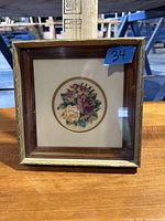Front view of framed flower stitch embroidery artwork showing intricate multicolor floral embroidery inside square wooden frame with gold finish.