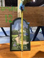 Framed canvas painting with gazebo and floral garden motif, showing arched top and dark green frame.