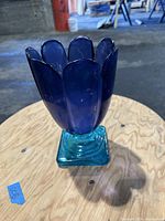 Front view of blue glass vase showing scalloped petal rim and square base on wooden surface.