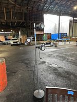 Full view of the three-light floor lamp in an industrial warehouse setting, showing the whole vertical pole and base with lights attached.