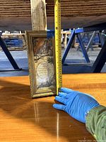 Vertical photo showing a gold ornate frame featuring leopard and globe art with tape measuring the height about 12 inches