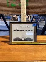 Framed print with front and side elevation views of Les Halles de Paris placed on wooden table with measuring tape showing width around 14.5 inches.
