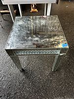 Front view of mirror glass table showing reflective surface with some wear and small chip noted.