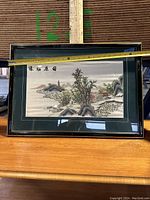 Framed Asian landscape picture with black frame and green double matting, shot with horizontal measuring tape to confirm size.