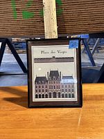 Frontal view of framed Place des Vosges art print on wooden surface showing the artwork and frame.