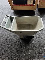 Photo showing side view of light gray plastic wheelbarrow, highlighting its bucket, handles, and single wheel.