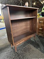 Front angled view of wooden shelving unit showing three shelves and scratches on surface.