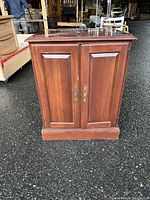 Front view of small wooden cabinet with closed double paneled doors and brass-tone handles.