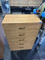Front view of tall dresser showing wood grain melamine finish and five drawers with matching handles.