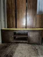 Front view of the wooden TV stand showing two cabinet doors with textured patterns and two open shelves in the middle. Measuring tape on top indicating width.
