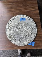 Photo of the circular welcome sign featuring a rooster and 'WELCOME TO OUR HOME' text on a wooden table, showing full front view.