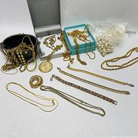 Collection of goldtone costume jewelry necklaces and boxes displayed on white surface with some necklaces loose and some in jewelry boxes, also bag of faux pearls visible.