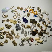 Top view of 36 pairs of costume jewelry earrings in various styles and colors laid out on a white background