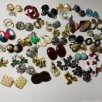 Top-down view of 40 pairs of assorted costume jewelry earrings arranged in rows, showing wide variety of colors and shapes.