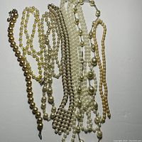 Top view of ten different faux pearl costume jewelry necklaces laid out showing variety in bead size, color and arrangement.