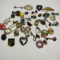 Multiple costume jewelry pins and hair clips arranged in rows on white background. Items include bows, hearts, flowers, flags, sunglasses, and more, made of various metal tones and colorful embellishments.