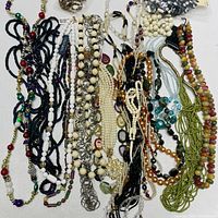 Full view of all costume jewelry beaded necklaces laid flat on a white surface, showing multiple colors and bead types, including long strands, seed beads, and metal chain links.