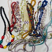 Overview of multiple costume jewelry necklaces laid flat showing variety of colors, beads, and materials.