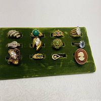 Front view of 11 assorted costume jewelry rings displayed on green velvet stand.